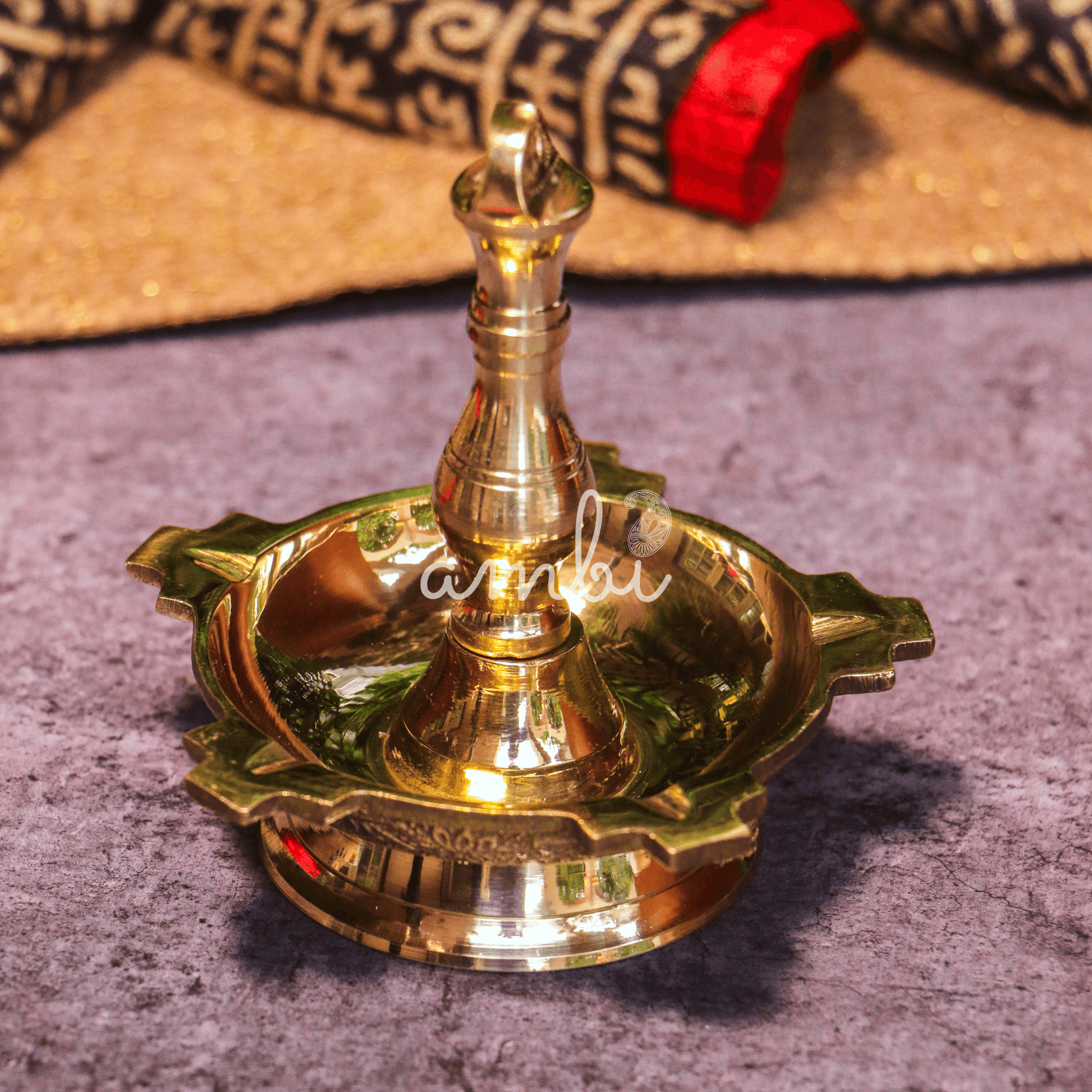 Brass oil lamp on a textured surface with 'Ambi' branding.
